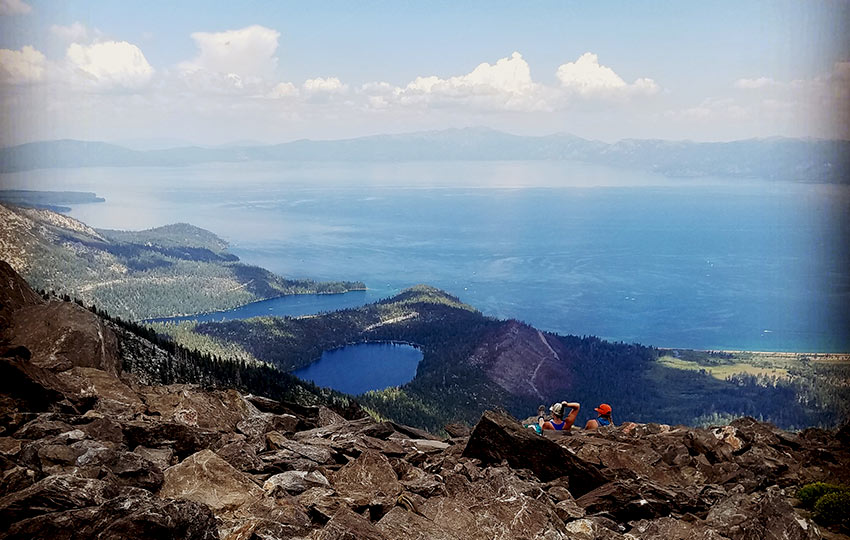 Hikers enjoying views of multiple small lakes in addition to Lake Tahoe on a partially cloudy day