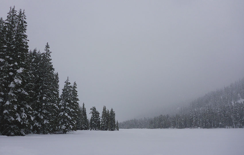 Overcast skies and as snow-covered lake flanked by forests