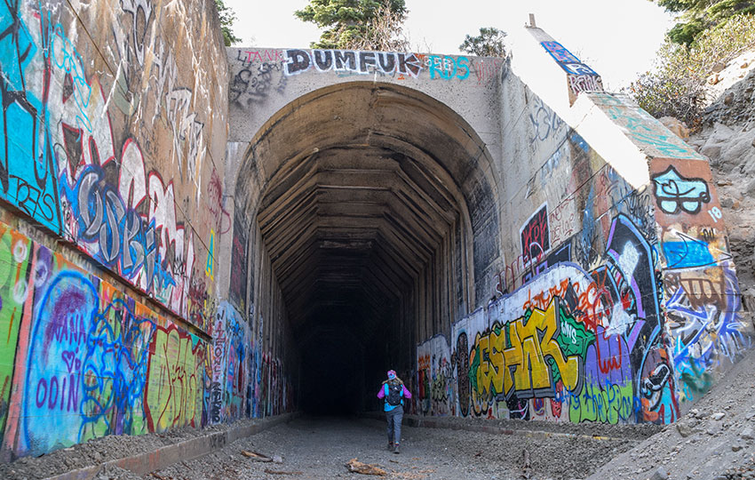 Hiker beginning to walk into an old train tunnel covered with graffiti art