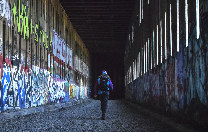 Hiker walking through old train tunnels with graffiti on the walls