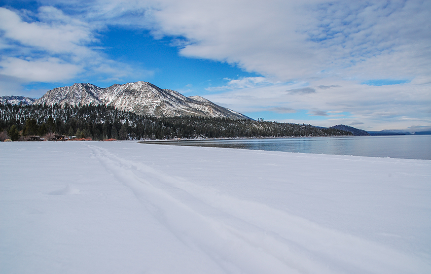 Clouds, blue skies, a mountain range, and snow on the beach